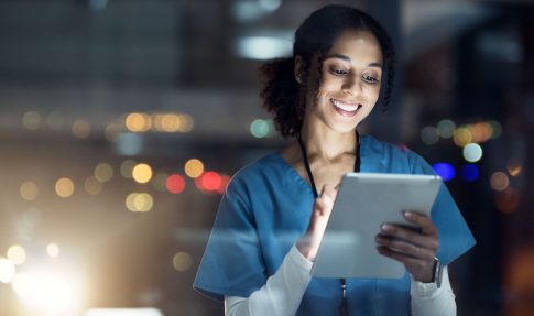 Woman in medical scrubs smiling while looking at tablet screen.