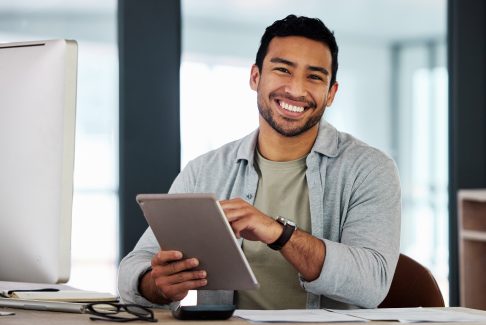 Man smiling in office while working on his tablet at his desk.